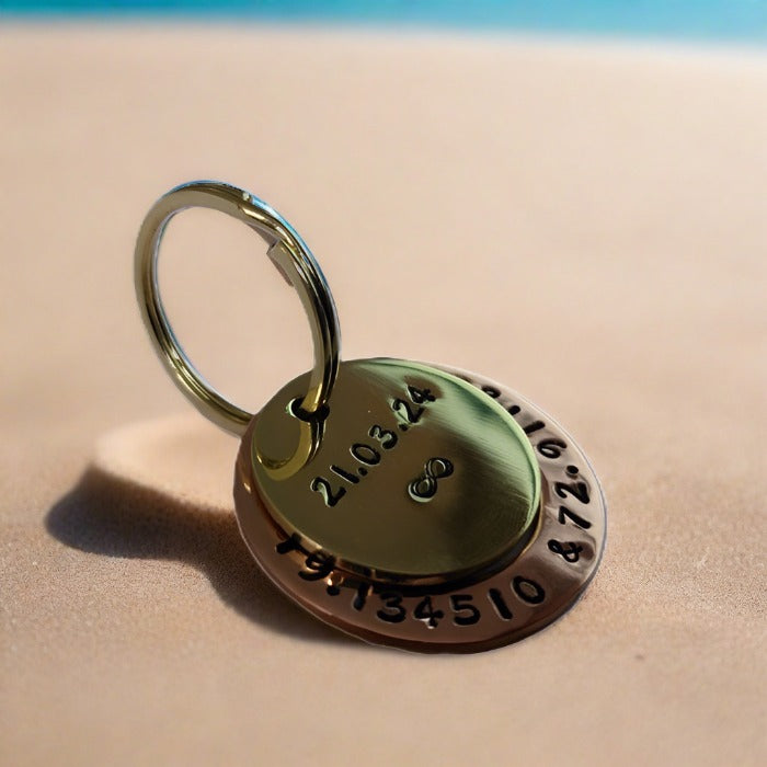 Hand-stamped brass and copper keychain personalized with a custom date and infinity symbol, shot on sand