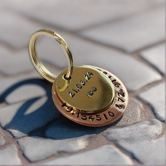 A hand-stamped brass and copper keychain with personalized text on the surface, placed on a stone texture background.