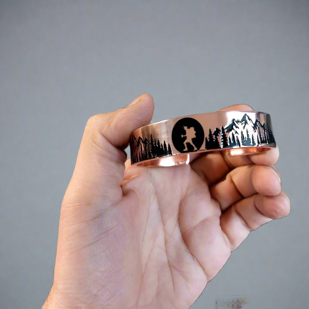 Hand holding a copper bracelet with nature-themed engraving in front of a keyboard.