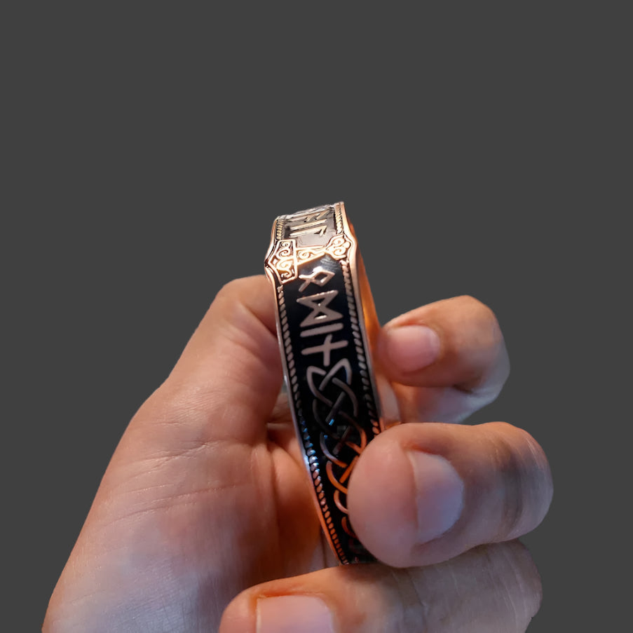 Hand holding a decorative bracelet with intricate designs on a blurred background