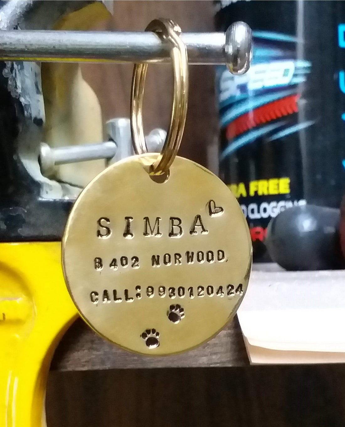 Hand-stamped brass pet tag personalized with pet name and contact details, hanging in a workshop setting
