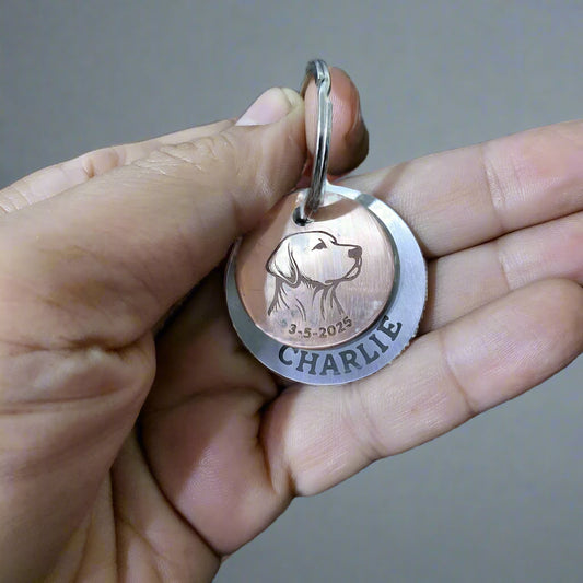 Hand holding a pet tag with a dog's name and date engraved, against a keyboard background.