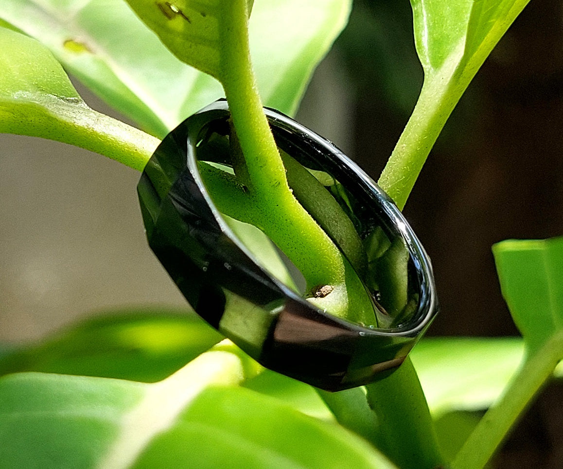 Classic Wide black ceramic ring nestled among green leaves, outdoor lifestyle shot