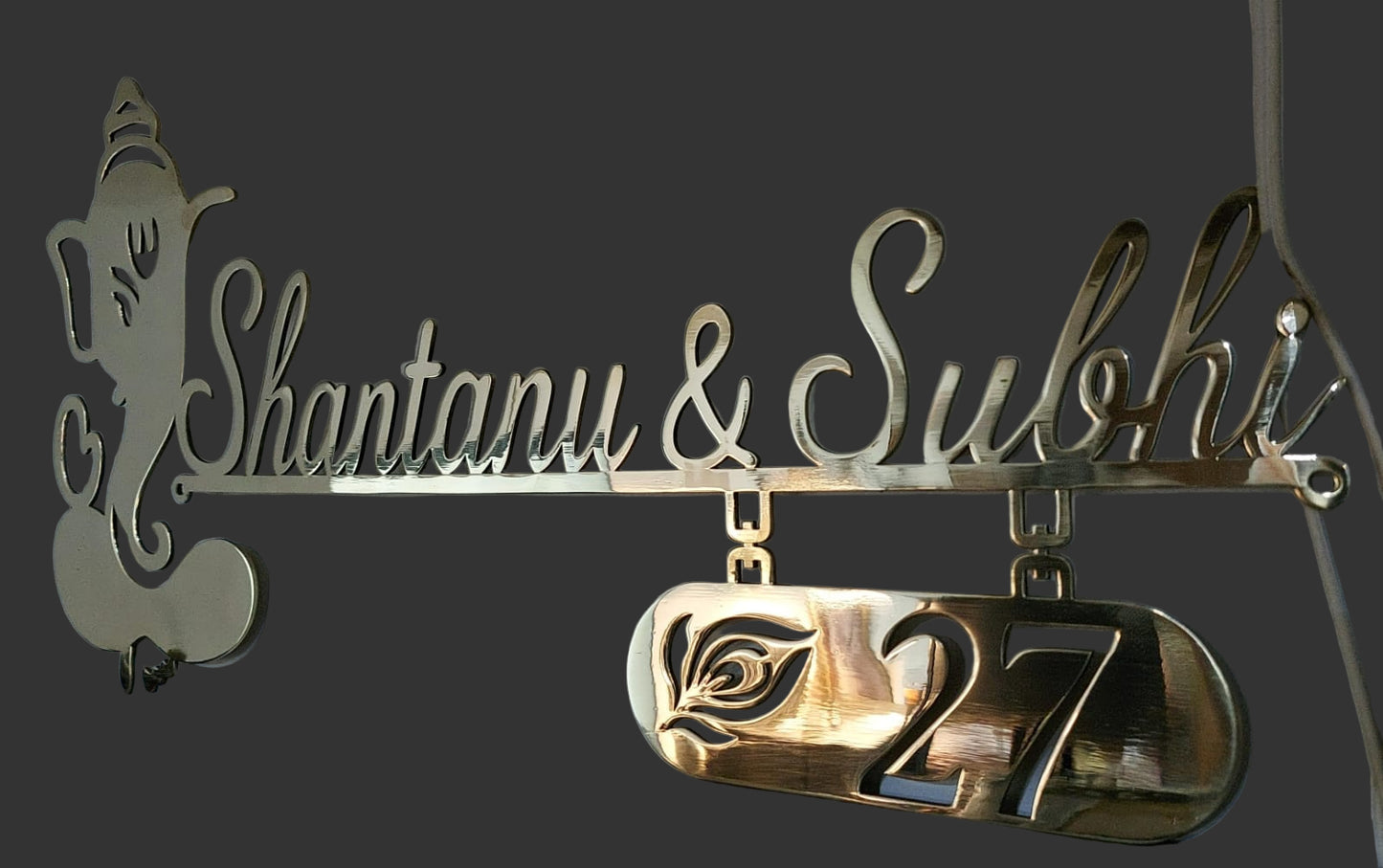 Decorative metal nameplate with 'Shantanu & Sulohsi' and number '27' on a white background