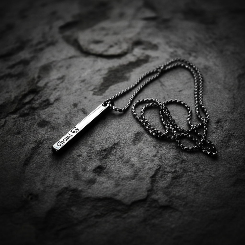 Stainless steel personalised bar pendant necklace on dark charcoal surface with moody dramatic lighting